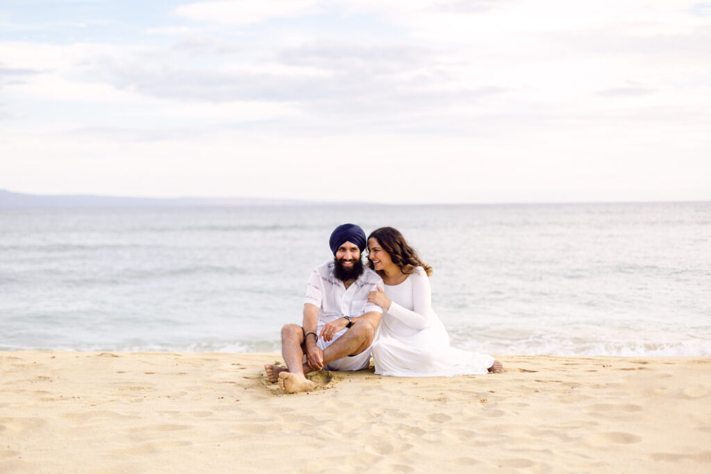 Couple sitting on sand posing for Hawaii beach babymoon photography session
