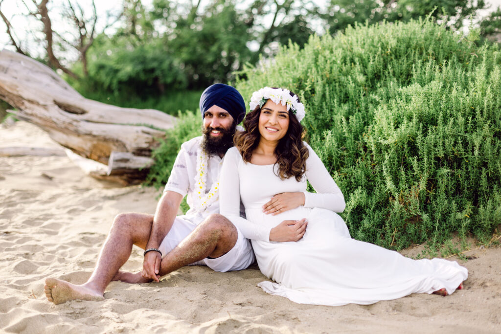 Couple with lei sitting in sand on beach for sunset maternity babymoon photography