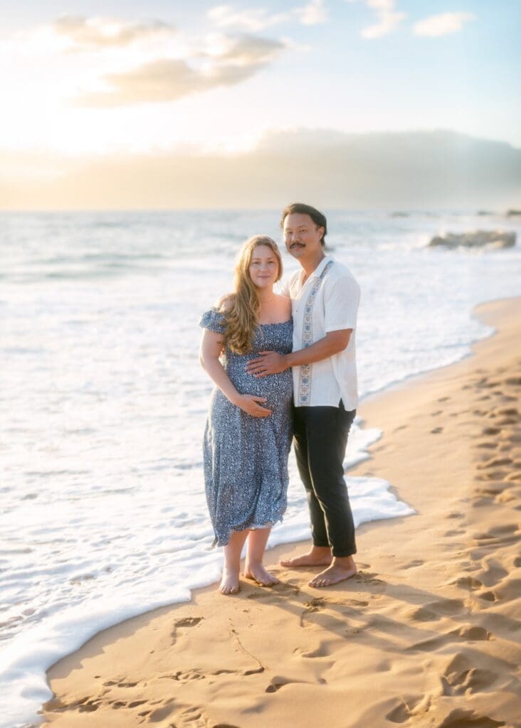An expectant couple walking along the golden sand of Mokapu Beach with the tropical landscaping of the Andaz Maui in the background for their maui maternity photos
