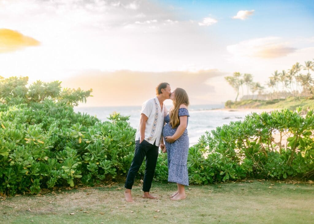 A babymoon couple sharing a kiss among the lush, manicured tropical palms and landscape of the Andaz Maui at Wailea Resort