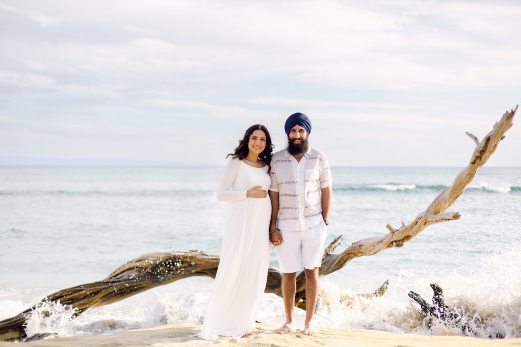A babymoon couple holding hands and splashing in the gentle shoreline waves at Ukumehame Beach in West Maui