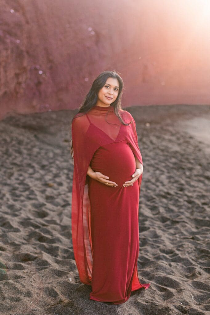 Pregnant woman in burgundy dress black sand beach Maui maternity photos