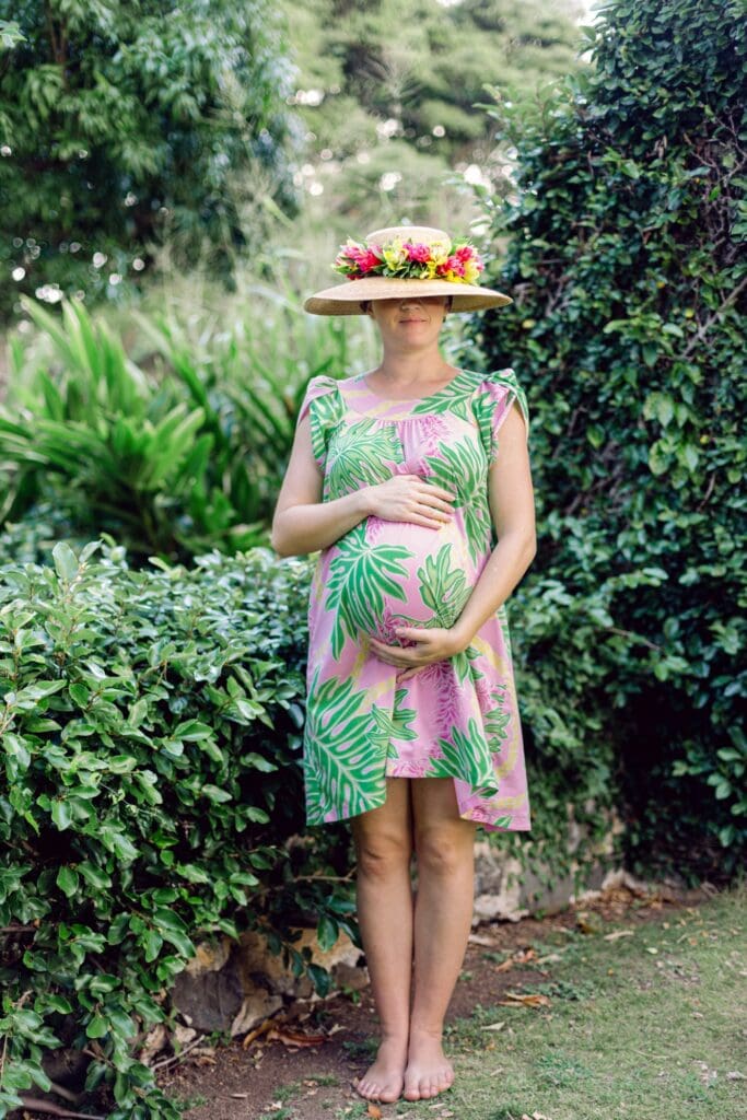 Maternity portrait in a Maui botanical garden featuring tropical flowers, an expectant mother wearing a sun hat and a floral crown.