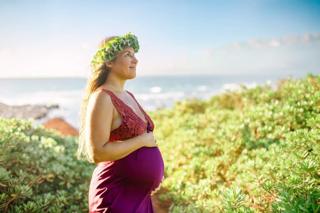 A maternity portrait of an expectant mother wearing a custom naupaka head lei against red sand beach