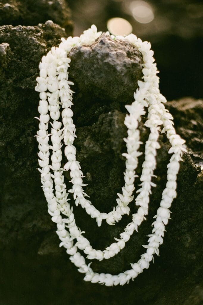 Close-up detail of a white floral lei resting on dark volcanic rock during a sunset maternity session at La Pérouse Bay, Maui.