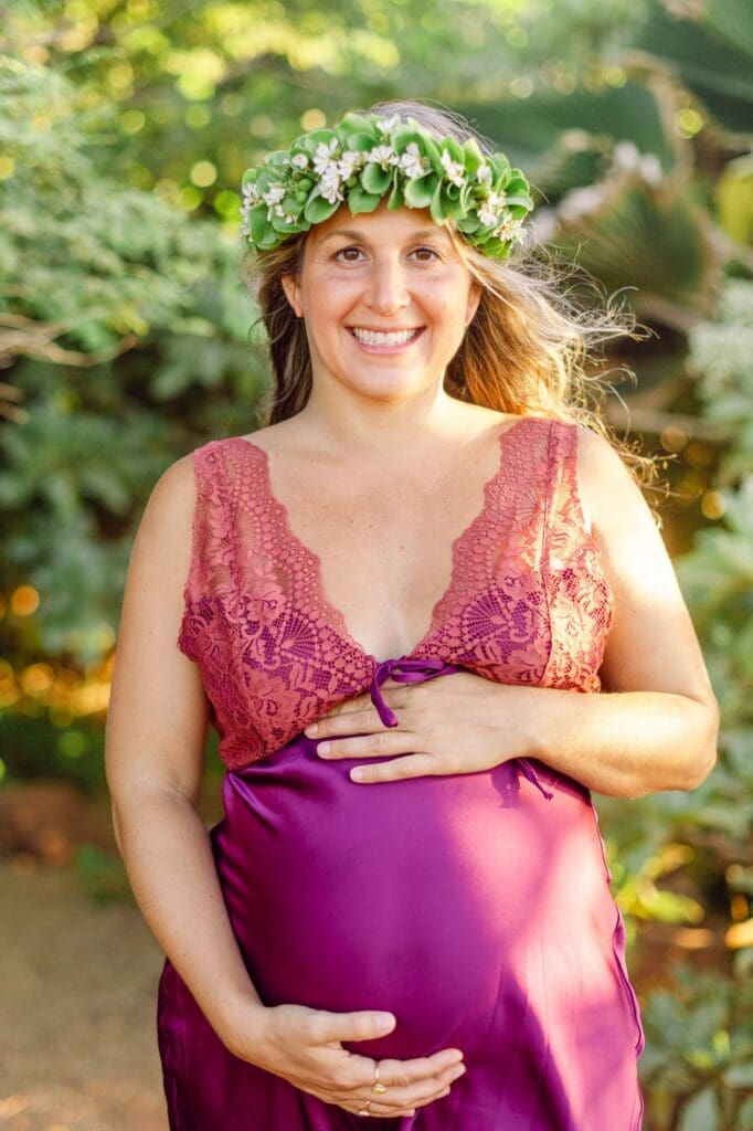 portrait of pregnant woman holding belly with wind-swept hair and naupaka head lei on Maui