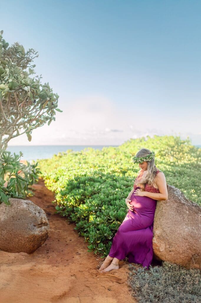 pregnant woman sitting on coastal boulder surrounded by naupaka on Maui red sand beach