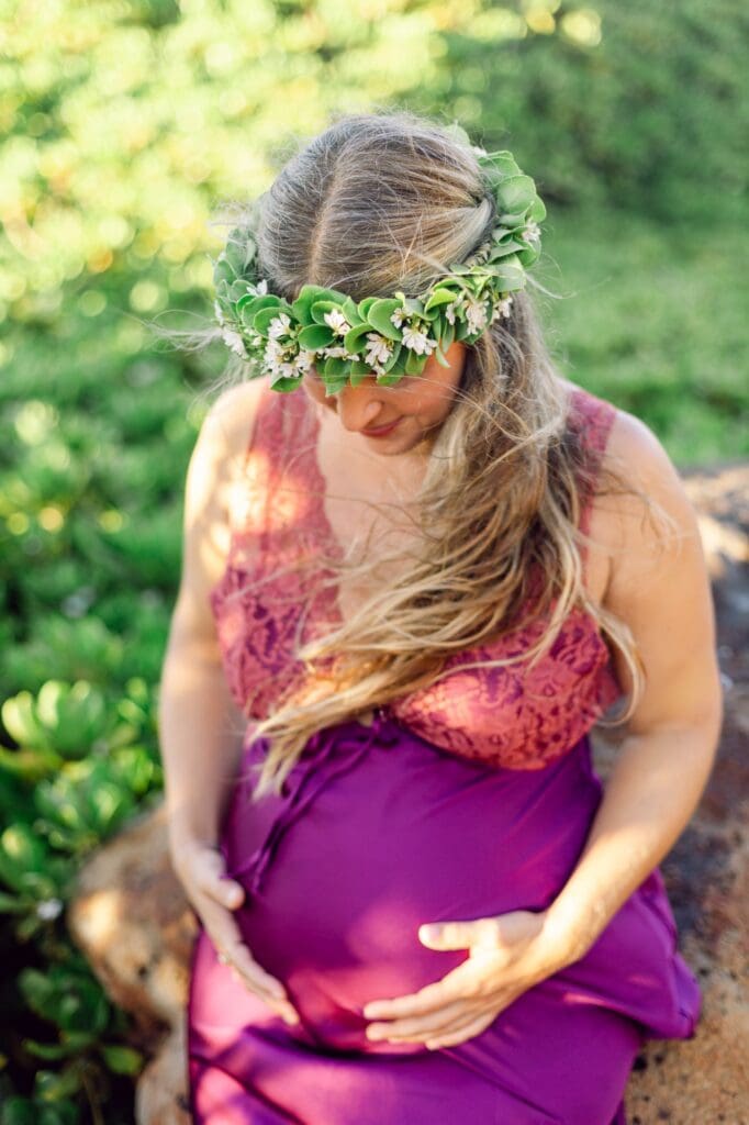 pregnant woman sitting and looking at her baby bump on Maui North Shore beach