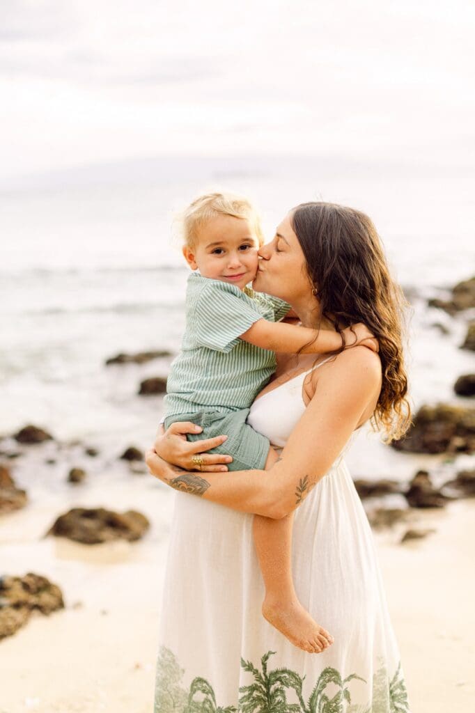 mother picking up toddler for hug and kiss on Maui beach during maternity photo session