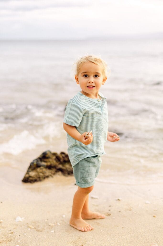 toddler playing with seashells on Maui beach during family maternity photo session