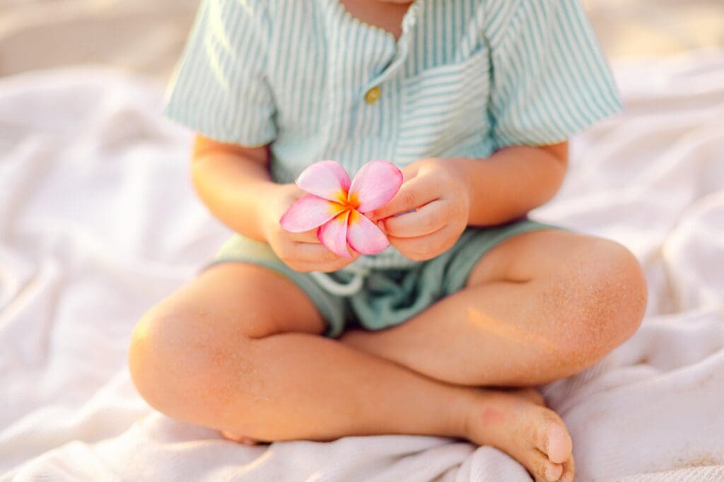 toddler holding pink plumeria flower for baby during Maui maternity photo session