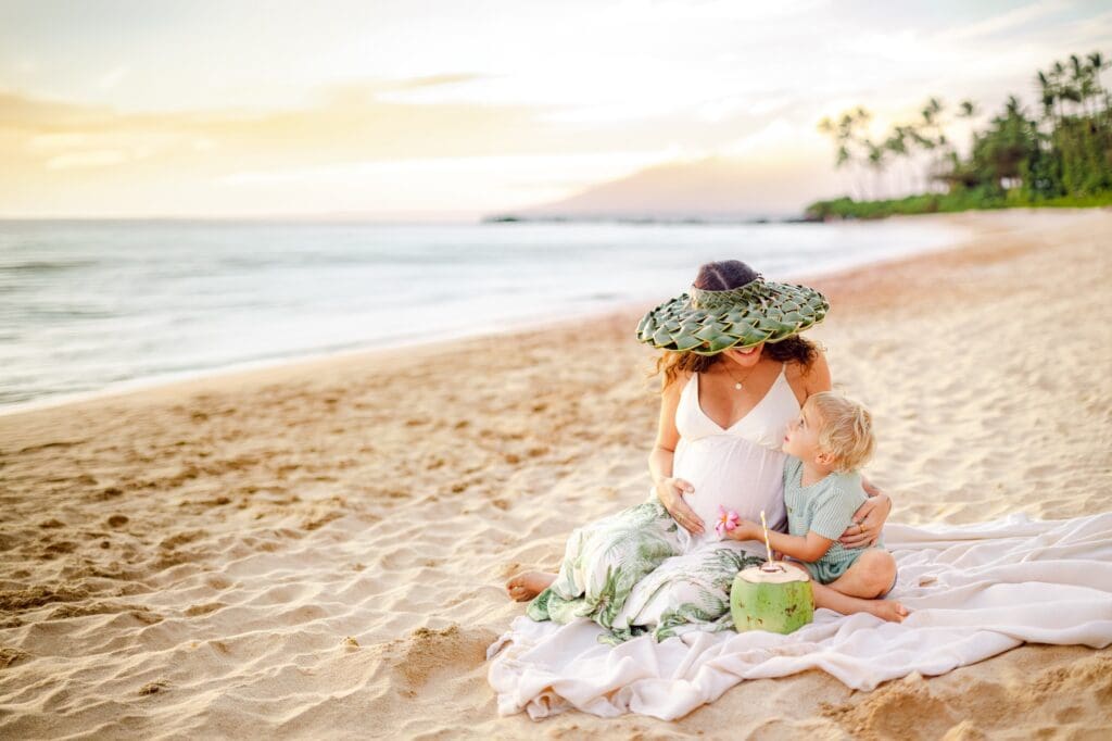 toddler touching pregnant belly with plumeria flower during Maui wailea maternity session