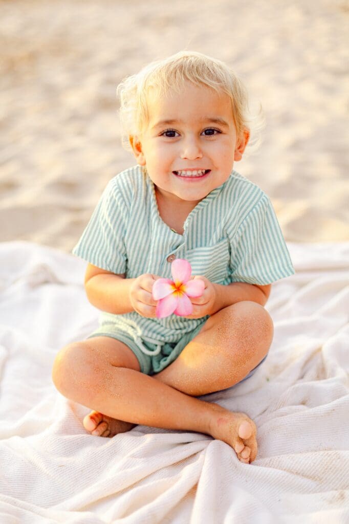 Close-up of a toddler holding a pink plumeria for the baby during Maui maternity photos.